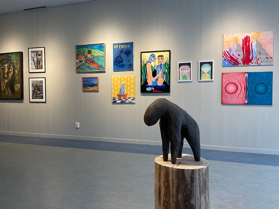Utsiktsbild över utställningshall med skulptur i förgrunden och tavlor på vägg i bakgrunden